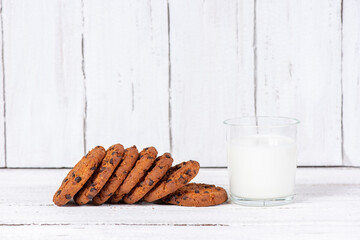 Delicious homemade cookies with chocolate and a glass cup of milk on a wooden table. Beautiful still life