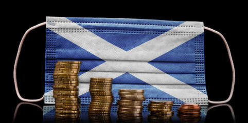 Medical mask with the flag of Scotland behind some shrinking stacks of various coins.(series)