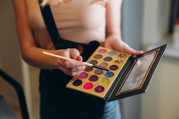 Multi-colored eyeshadow palette close-up. Makeup artist taps the eyeshadow with a brush