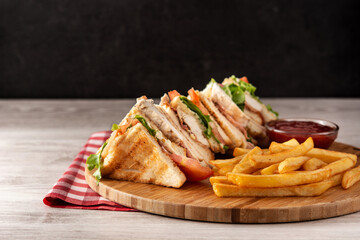 Club sandwich and French fries with ketchup sauce on wooden table