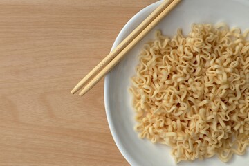 Instant noodle in white plate with bamboo chopsticks on wooden table.