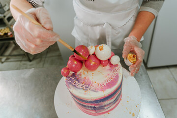 Female confectioner decorating birthday cake using edible golden dye and brush
