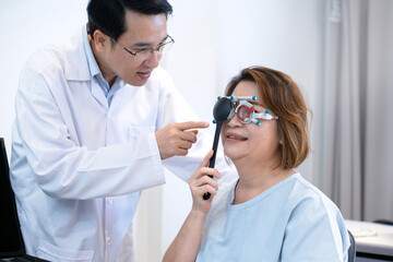 Senior Asian female patient holding  occluder to covering one eye to check her vision, optometrist advises her nearby