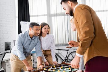 Multicultural business people looking at each other near table soccer in office