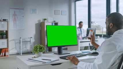 African American Medical Doctor is Making a Video Call with Patient on a Computer with Green Screen Display in a Health Clinic. Assistant in Lab Coat is Talking About Health Issues in Hospital Office.