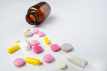 Multicolor pills and tablets spilling out from glass pill bottle on white.