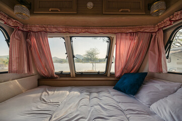 Inside of empty bed in camper van and the view through window with curtain on lakeside