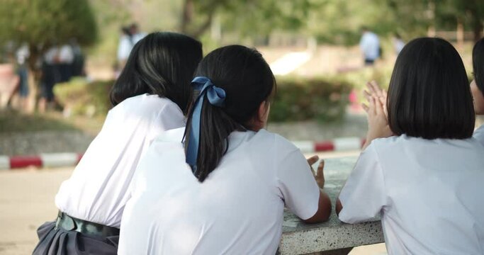 Back view of female Asian high school students in white uniform waiting for the school shuttle or waiting for their parents to pick them home in the evening after school.