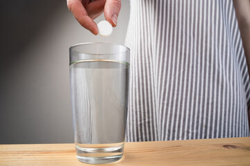 Close up sparkling water glass with dissolving effervescent aspirin pill standing on wooden table