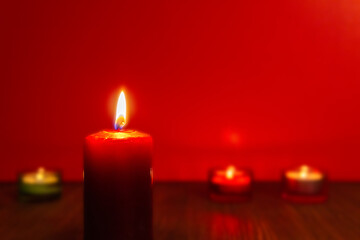 Obraz na płótnie Canvas Burning red candle and other candles on red background