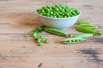 Fresh green peas in bowl and pods placed on wooden board