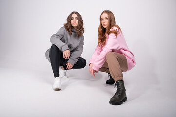 Full length view of two young girls in sports fashionable clothes sit on their haunches on a white background. People fashion lifestyle concept.