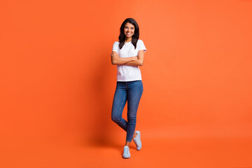 Fototapeta na wymiar Full length photo of self-assured lady crossed hands wear white t-shirt jeans sneakers isolated orange color background