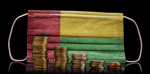Medical mask with the flag of Guinea-Bissau behind some shrinking stacks of various coins.(series)