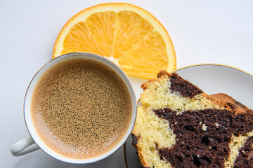 Piece of homemade chocolat-orange cake decorated with orange slice and a cup of espresso coffee on a white background.