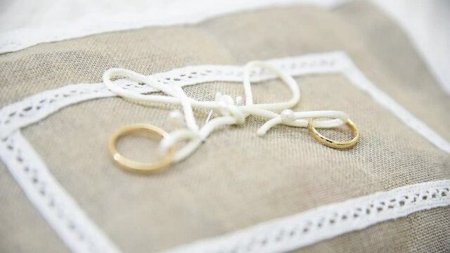 Gold wedding rings with a white bow on a brown cloth. Two wedding bands on a textured brown fabric. Accessories for the wedding day. Two gold rings illuminated by sunlight

