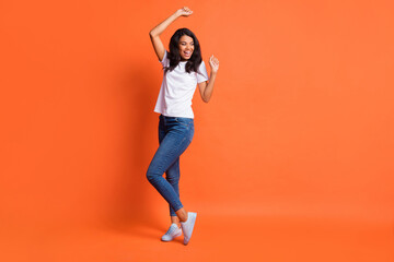 Fototapeta na wymiar Full length photo of girl dance look empty space wear white t-shirt jeans footwear isolated orange color background
