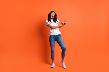 Full length photo of girl dance have fun wear white t-shirt jeans footwear isolated orange color background