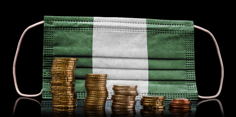 Medical mask with the flag of Nigeria behind some shrinking stacks of various coins.(series)