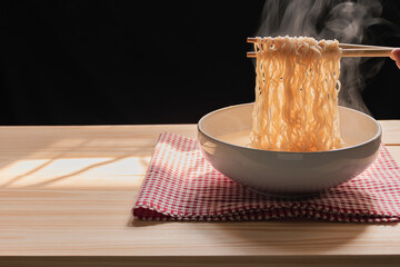 Steam and smoke Instant noodles in bowl on wooden table and nature light and black background, selective focus. It is a convenient and inexpensive food, but eating often is not good for health.