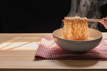 Steam and smoke Instant noodles in bowl on wooden table and nature light and black background, selective focus. It is a convenient and inexpensive food, but eating often is not good for health.