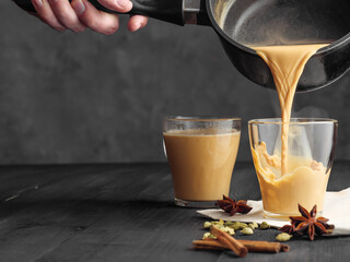 Hot masala tea is poured into a glass glass. Steam comes out of the mug. Gray background. Copy...
