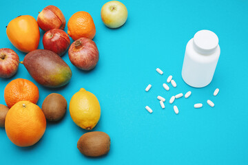 View from the top of white bottle with pills and many different fruits isolated on blue background.