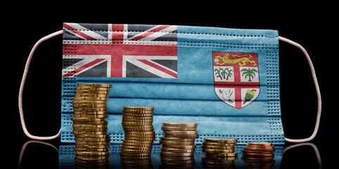 Medical mask with the flag of Fiji behind some shrinking stacks of various coins.(series)