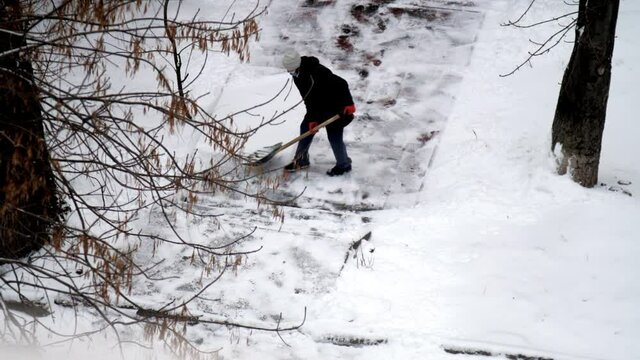 Person Cleans Snow From Sidewalk To House With Large Shovel Among Trees. Concept Harsh Weather Conditions