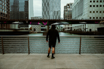 Caucasian male athlete jogging through city taking a breather by bridge 