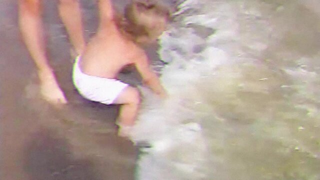 VHS footage from little happy boy run along the sand beach and smiling. Old home family movie of cute baby with mother playing and enjoying on sea beach.