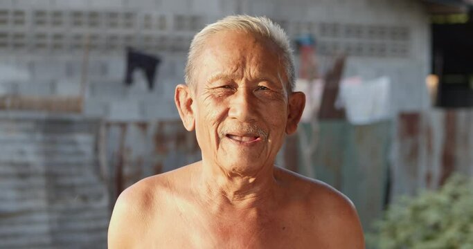 Slow motion scene of white-haired Asian elderly men do not wear clothes because of hot weather, poor status, older than seventy is laughing happily on the sunset light in the evening.