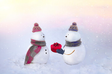 Snowmen in love wearing winter hats, scarves on a white background in pink and blue colors. Boy giving a gift to his girlfriend. Valentins day, love concept. 14th february.