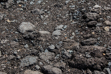 Broken road covered with old asphalt mixed with stones.