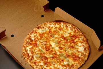 Pizza in a box on a black background. With cheese and mushrooms. Top view.