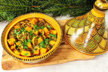 Moroccan vegetable tagine dish with aubergine and winter squash vegetables in open traditional tagine pot. Common yew foliage at the background.