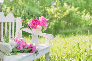 peony in jug on white wooden bench in summer garden