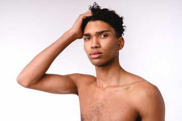 Fototapeta premium Attractive 20s african man touching his hair shirtless isolated over white background