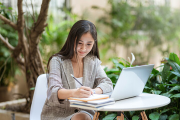 Image Asian businesswoman working taking notes with her laptop at home garden.