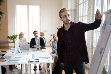 Startup leader presenting charts to his team in meeting room. Manager explaining sales reports on flipchart to employees. Corporate trainer giving marketing workshop to staff. Presentation concept