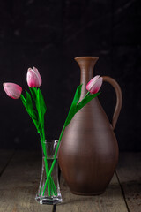 beautiful composition of fresh tulips in glass vase near clay jug on dark background, close view, Valentine day concept 