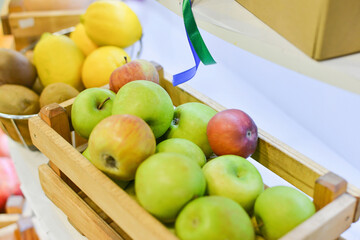 Fresh apples lie in a wooden box on the table with other fruits.