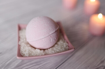 Pink bath bomb with sea salt in square bowl, pink candles on wooden gray bright bathroom table.