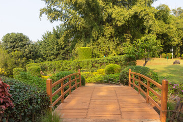 A wooden bridge with handrails over a stream in a park with lush green surroundings