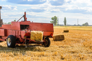 Fototapeta premium Harvester makes bales of straw at the agricultural field. Agricultural concept