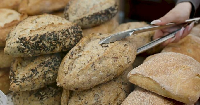 Buying bread at the store. A customer takes fresh bread with tongs at the bakery.