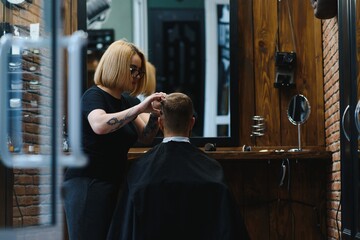 Stylish man sitting barber shop Hairstylist Hairdresser Woman cutting his hair Portrait handsome happy young bearded caucasian guy getting trendy haircut Attractive barber girl working serving client