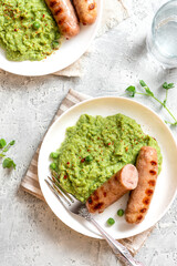 Pea mash and grilled sausages in a white ceramic plate on a gray concrete table top view. Tasty balanced lunch or dinner.