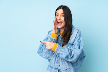 Young caucasian woman isolated on blue background pointing to the side to present a product and whispering something - obrazy, fototapety, plakaty