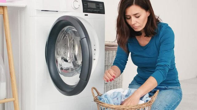 Woman loading items for washing into machine in laundry room